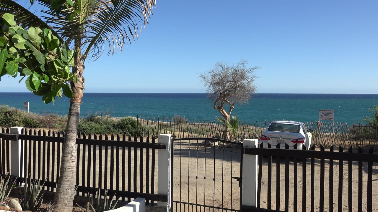 Gated yard with fence, trees, parked car, and blue water beyond.