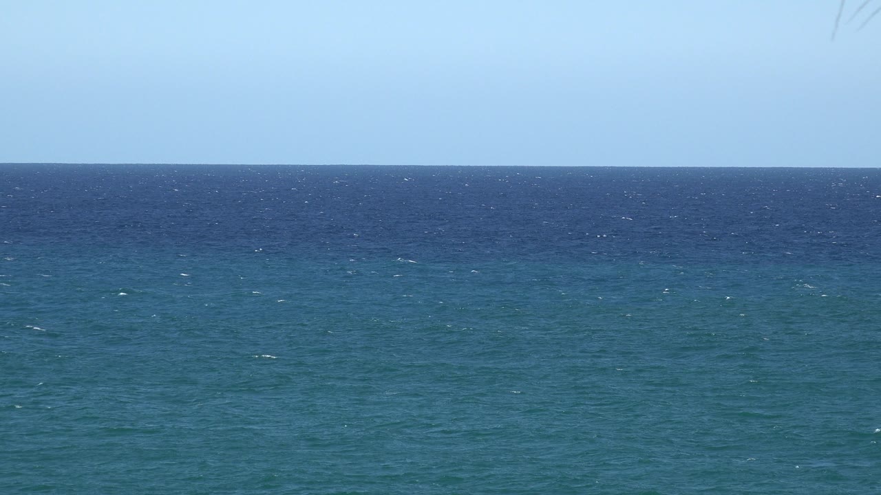 Blue-green water below a straight horizon and clear sky.