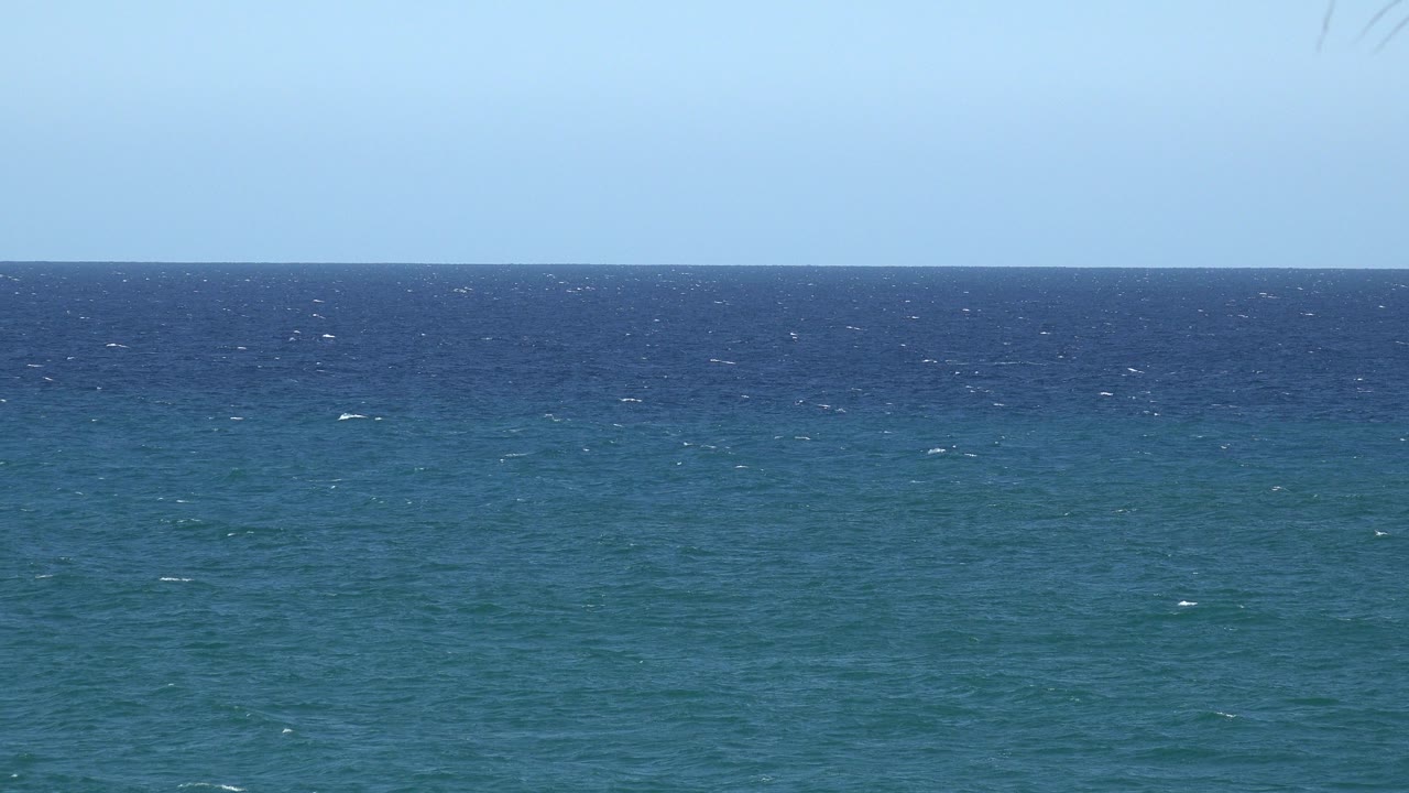 Blue-green sea under a pale blue sky with a level horizon.