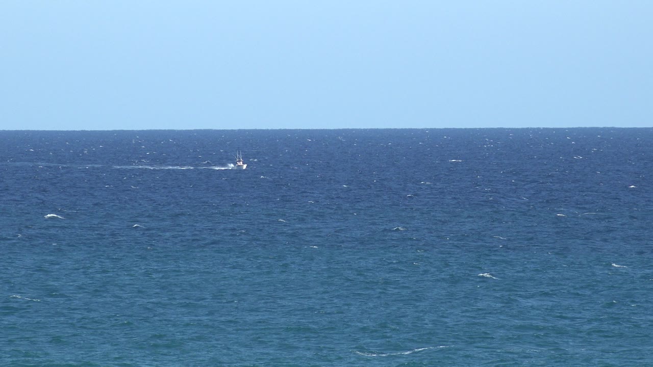Distant white boat on blue water beneath a pale sky.