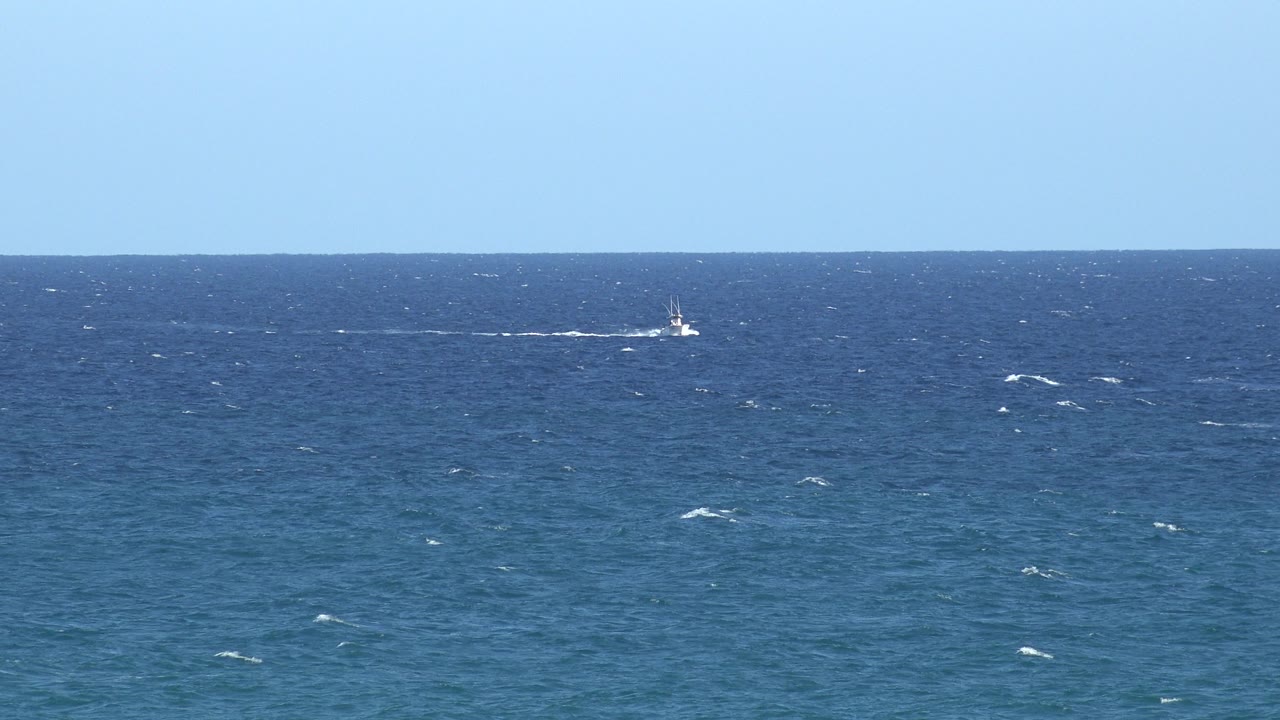Two distant boats on blue water with white wakes.
