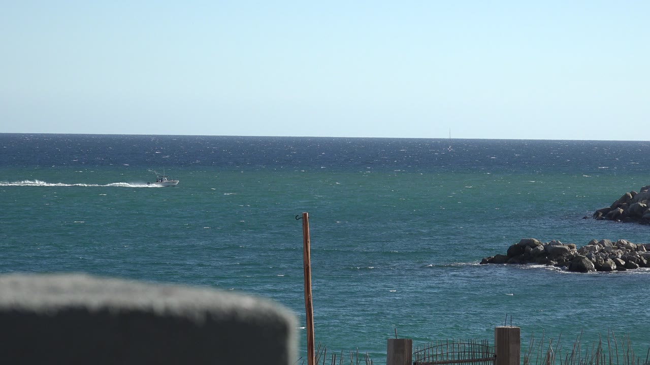 Small boat on blue-green ocean with rocks and shore foreground.