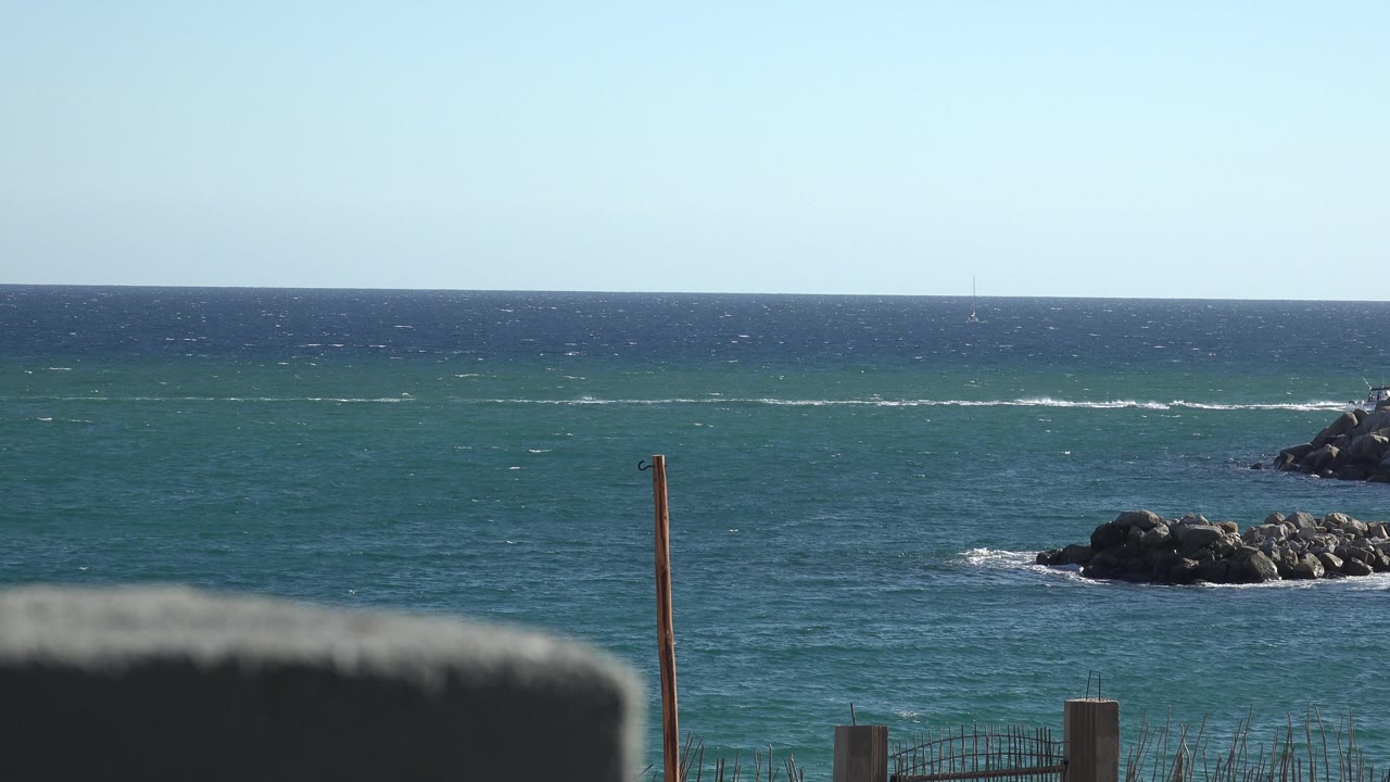 Rocky shoreline at right with blue sea and pale sky