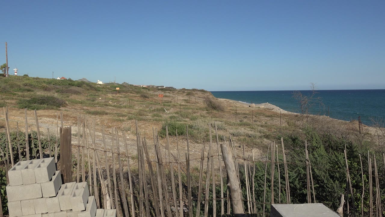 Dry grassy shoreline with rough fencing and blue sea beyond.