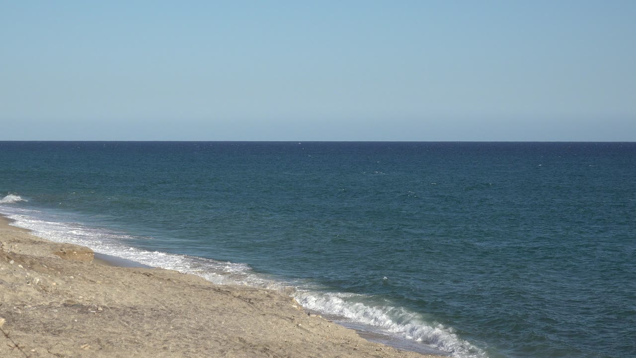 Wide ocean horizon with pale shoreline and small breaking waves.