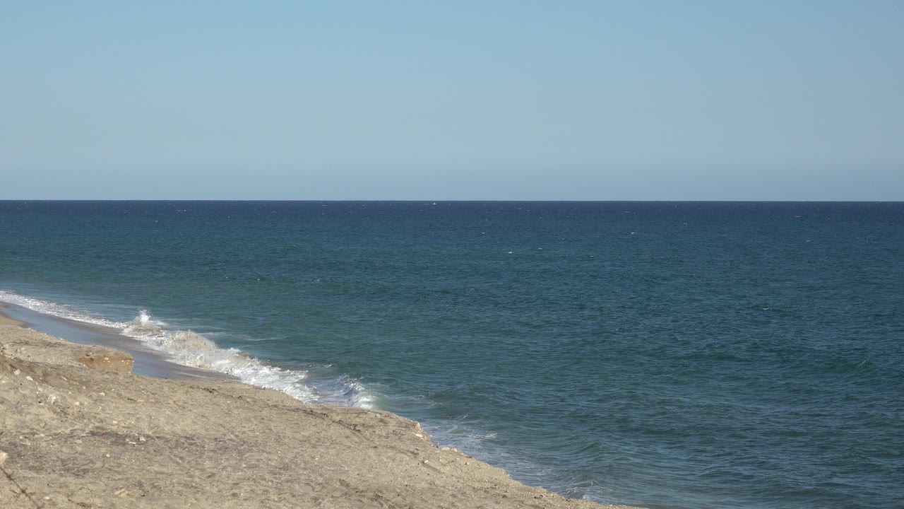 At 0:01, the Grand Junction Colorado 2017 footage shows a low wave curling onto the sand with open ocean behind it and no visible people.
