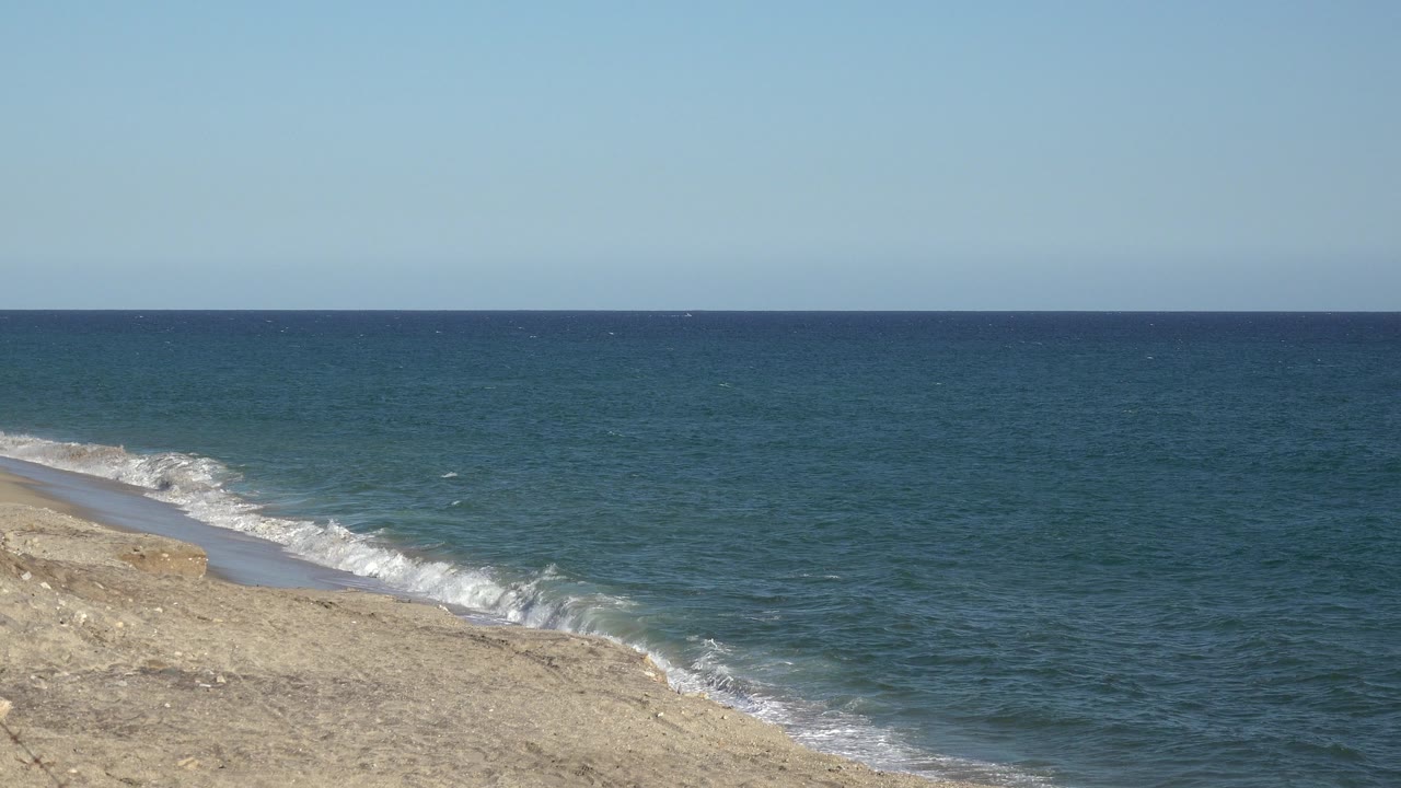 Sandy shoreline beside blue water under a clear sky