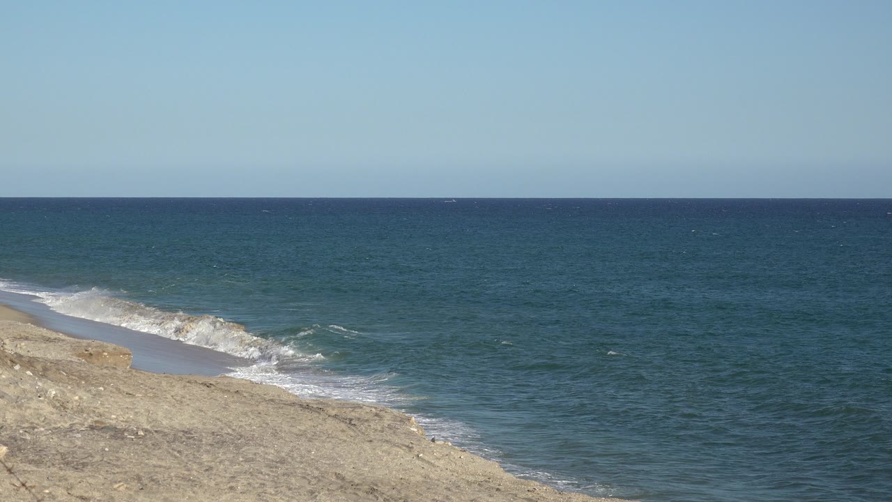 Sandy shoreline with small waves and open blue water.