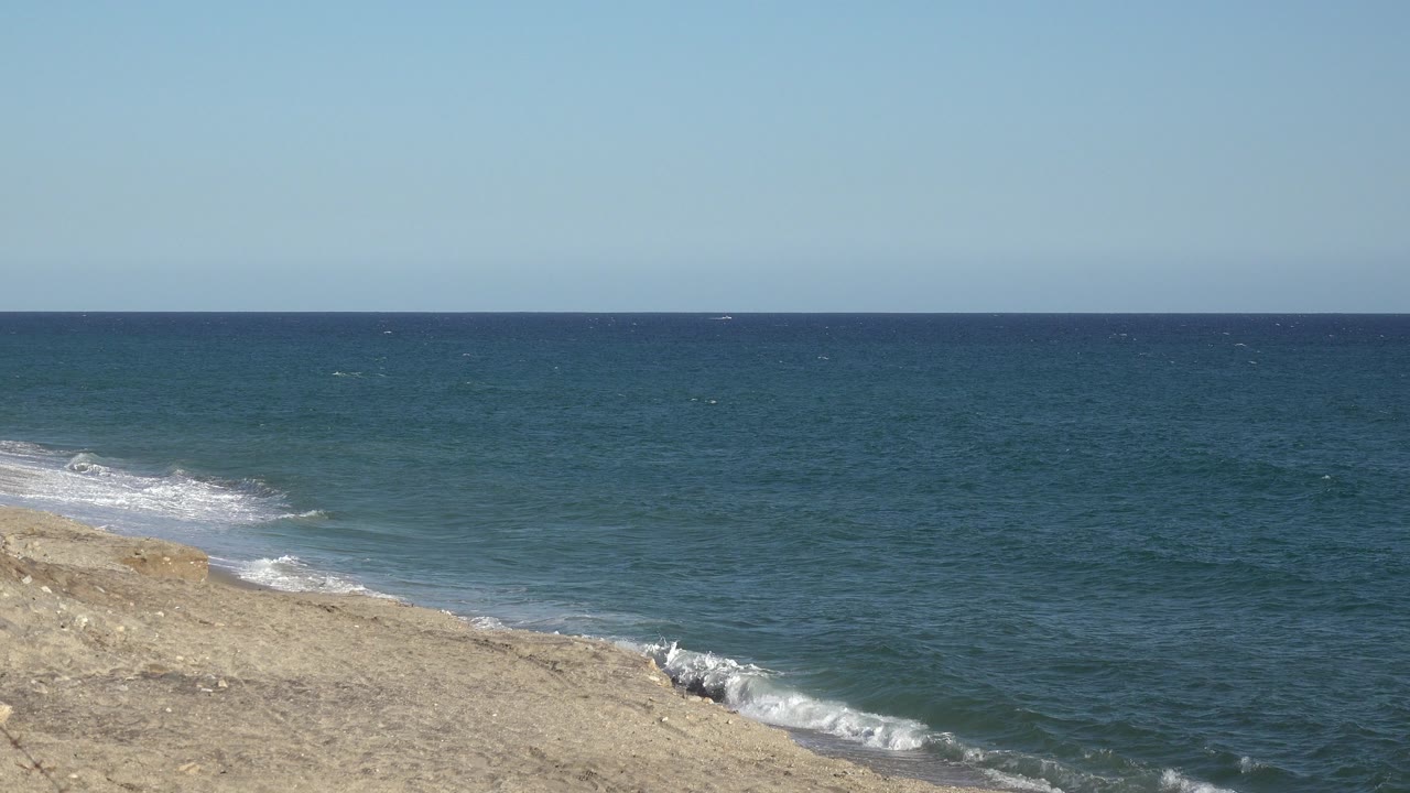 At 0:00, blue-green ocean water meets a pale sloping shoreline in the Grand Junction, Colorado 2017 clip, with a level horizon and no visible people.