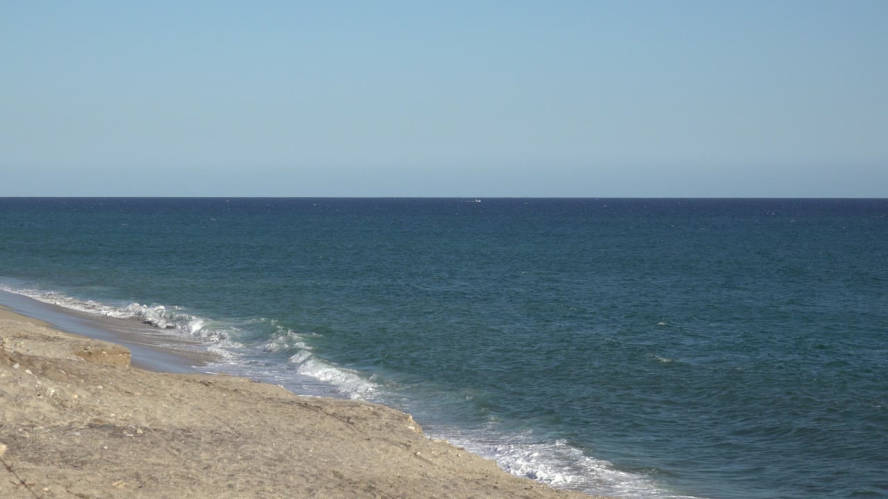 Blue ocean beside a pale shoreline under clear sky.
