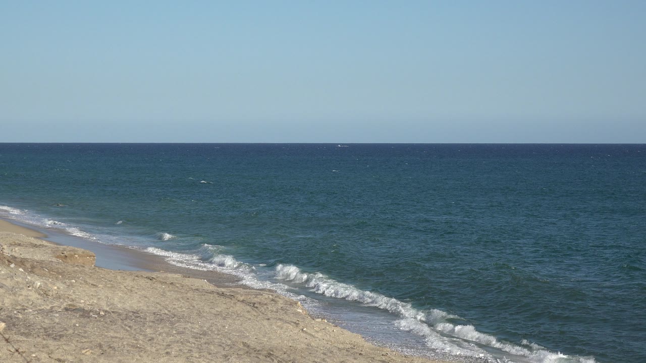 At 0:01, the Grand Junction, Colorado beach view shows white surf pushing farther up the diagonal sand line, with open blue-green water and no visible people.