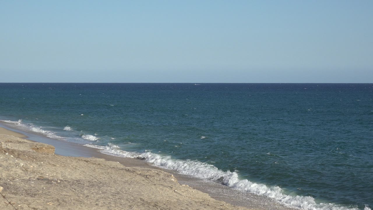 Foamy surf breaks along the beach with open water beyond.