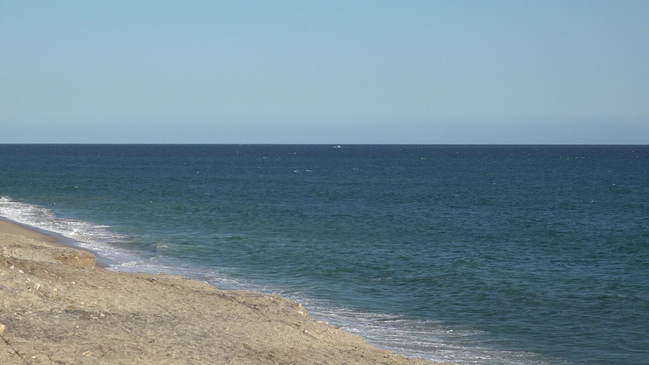 Blue sea beside a pale shoreline under a clear sky.
