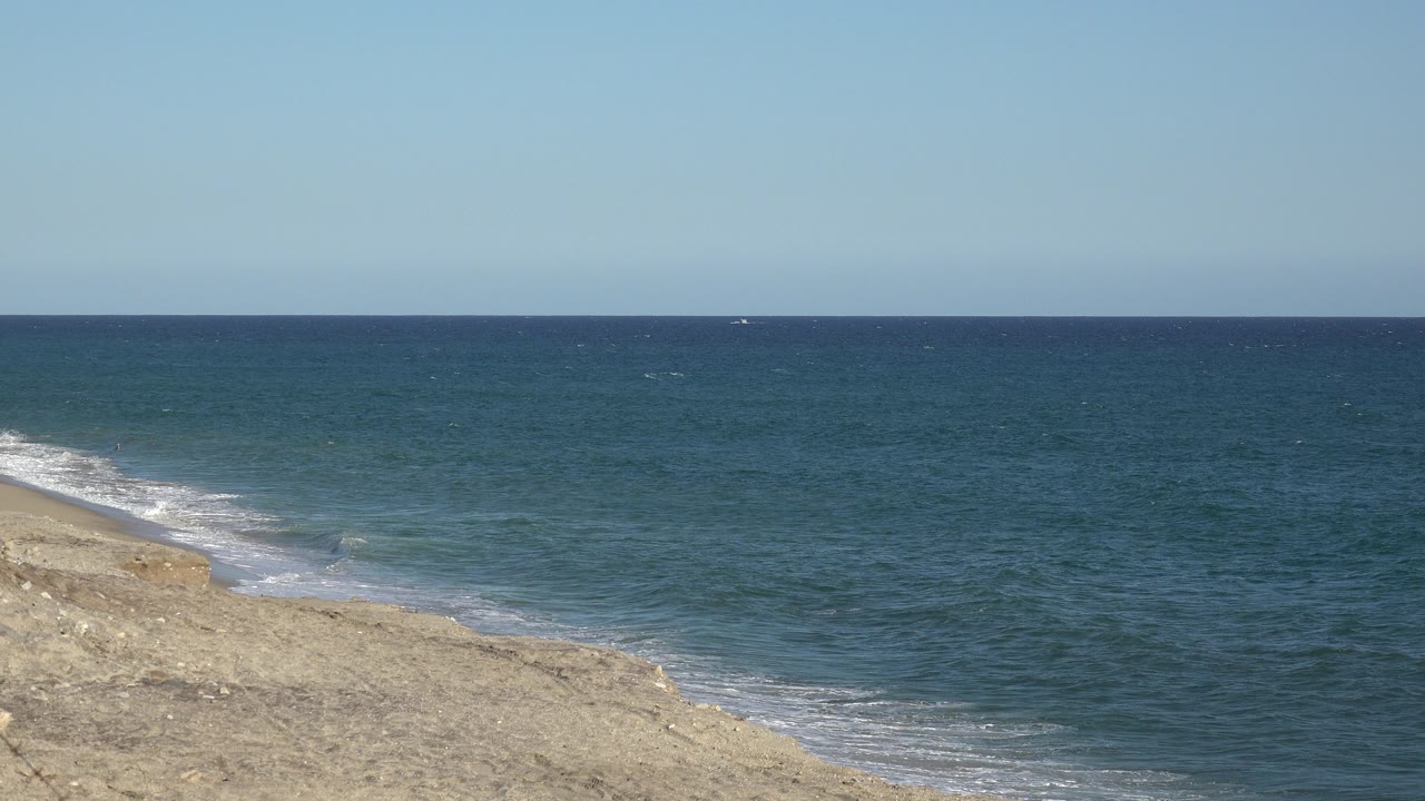The Grand Junction, Colorado frame shows small white surf reaching the pale shore while open blue water fills the midground and no visible people appear.