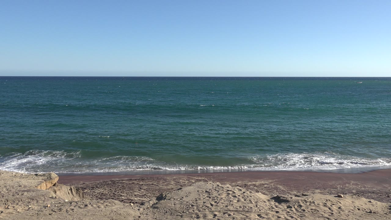 Wide beach view with waves, sand, ocean, and blue sky.