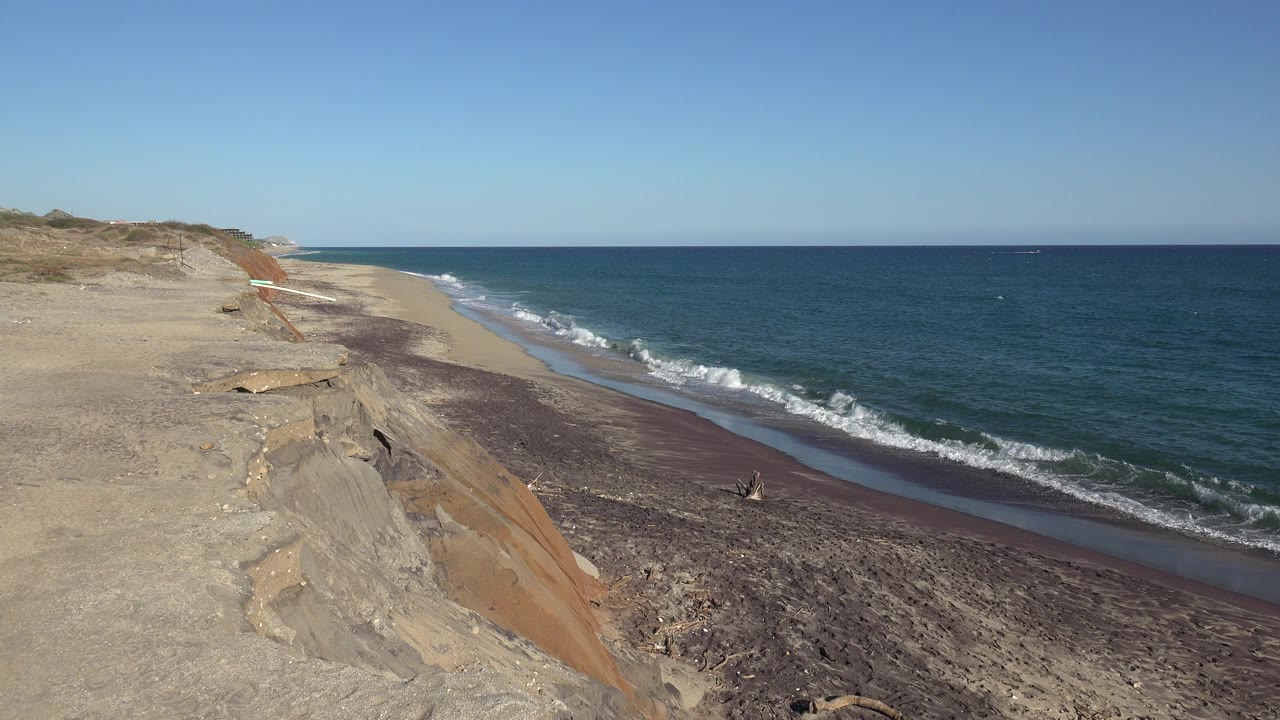 Eroded sandy bluff above a beach with surf and blue ocean.