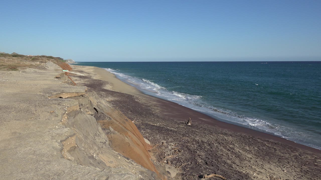Sandy bluff above a beach with ocean waves and a blue horizon.