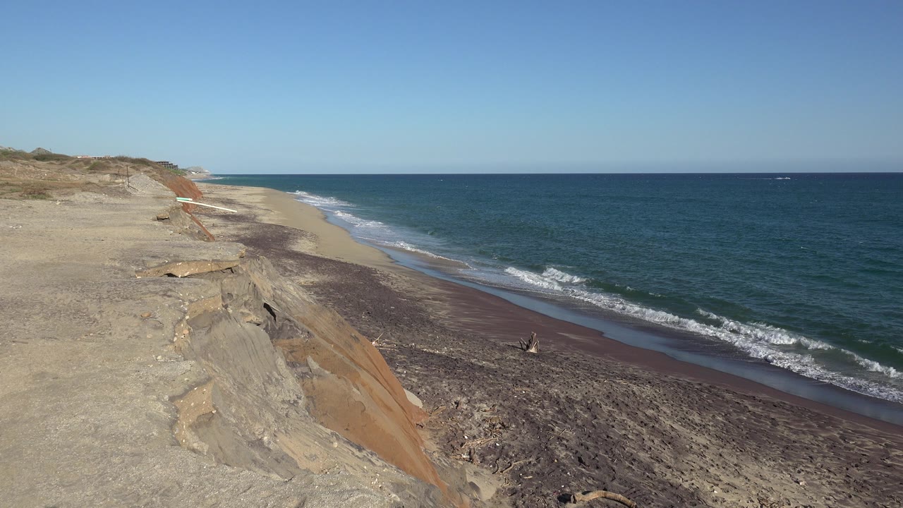 At 0:00, the Grand Junction Colorado clip opens on an eroded sandy bluff overlooking a dark stony beach, blue-green water, white surf, and no visible people.