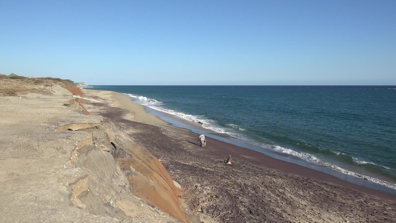 High view of sandy bluff, beach, waves, and a small person near the shore.