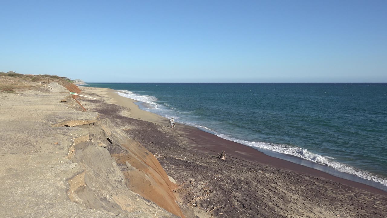 Eroded sandy cliff beside a beach with blue water and small waves.