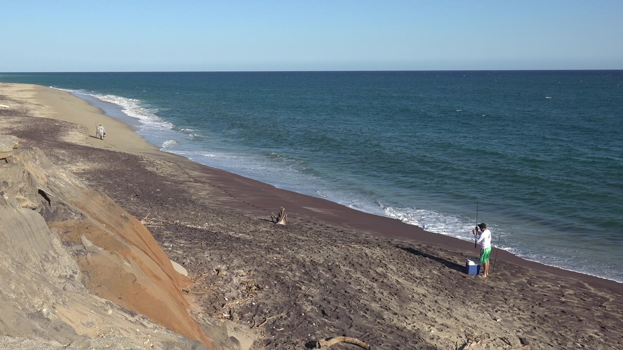 Person by blue cooler as small waves break along the beach.