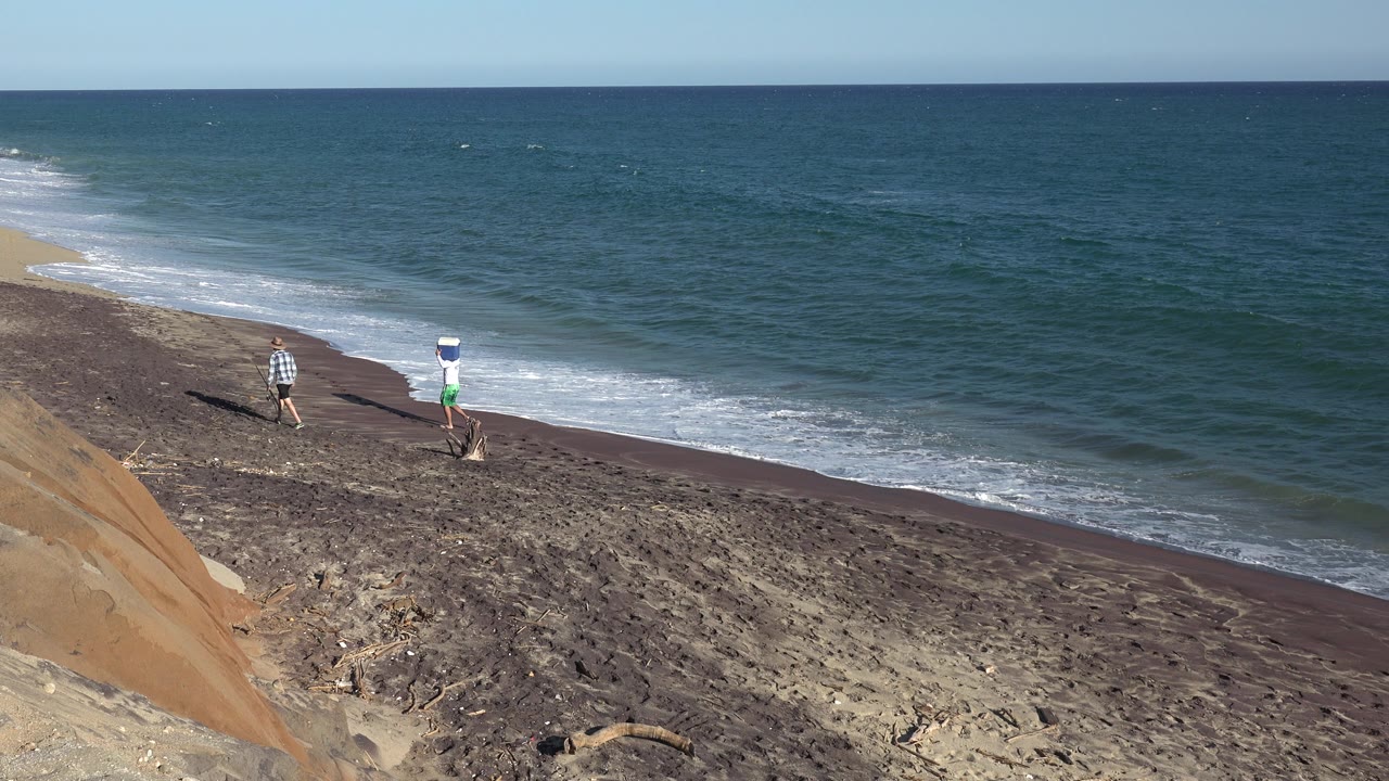 Two people walking on a sloped beach beside ocean waves.