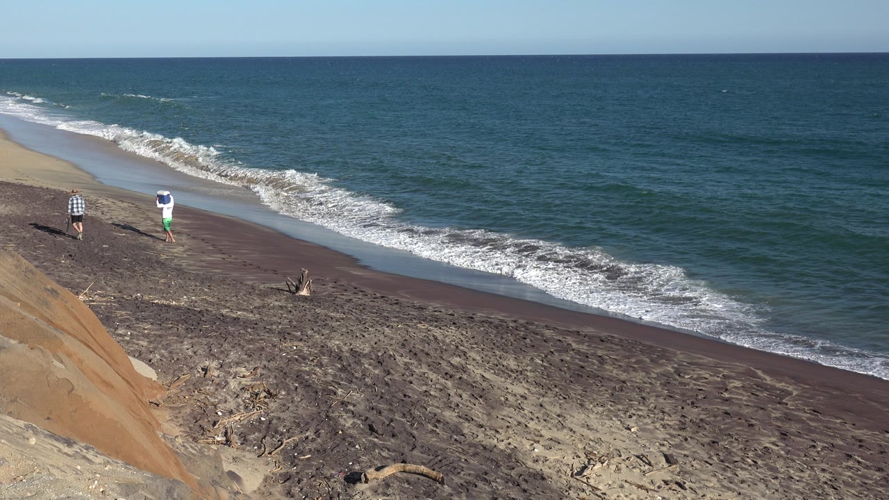 At 0:01, the two people remain near the left side of the Grand Junction, Colorado beach while white foam advances along the shoreline.