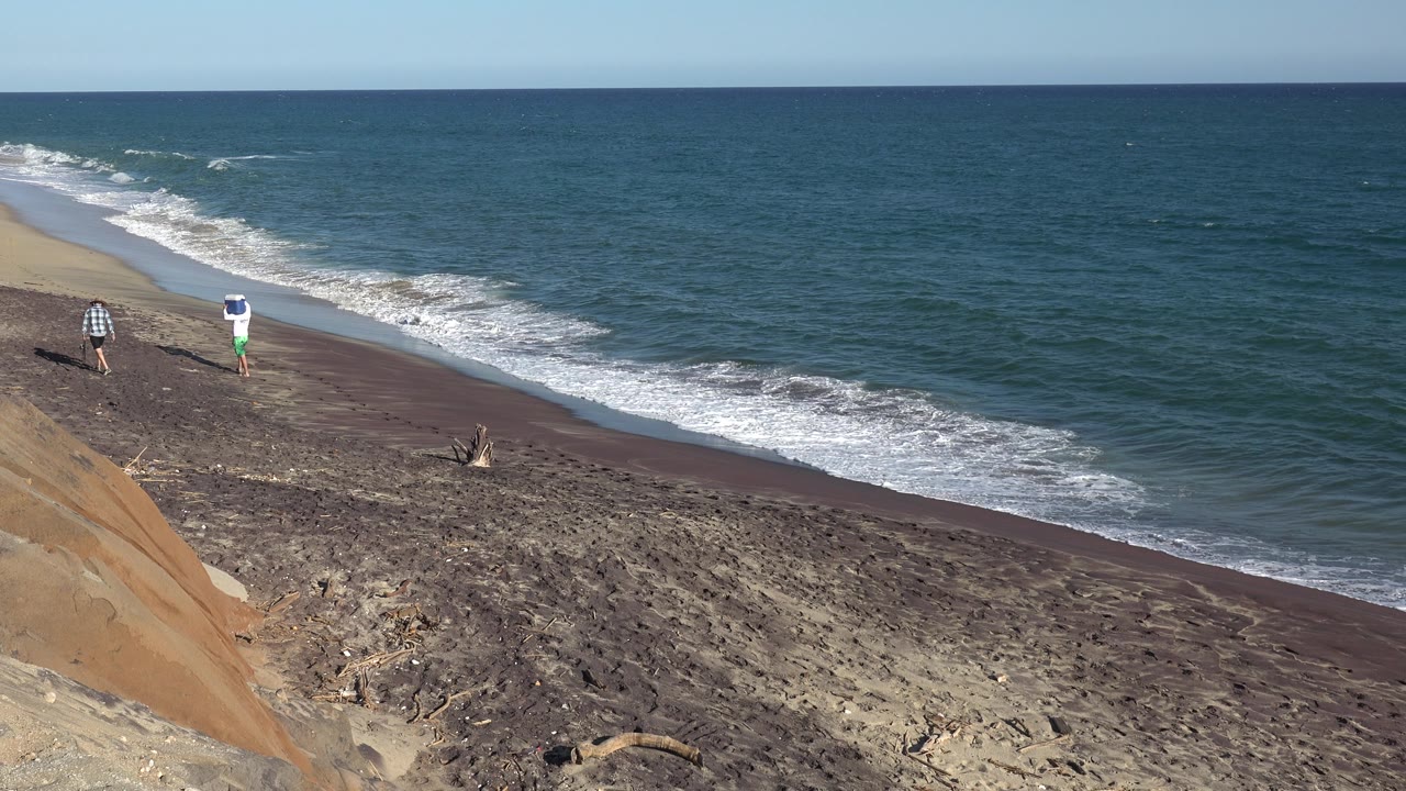 Two distant people walking beside a breaking wave.