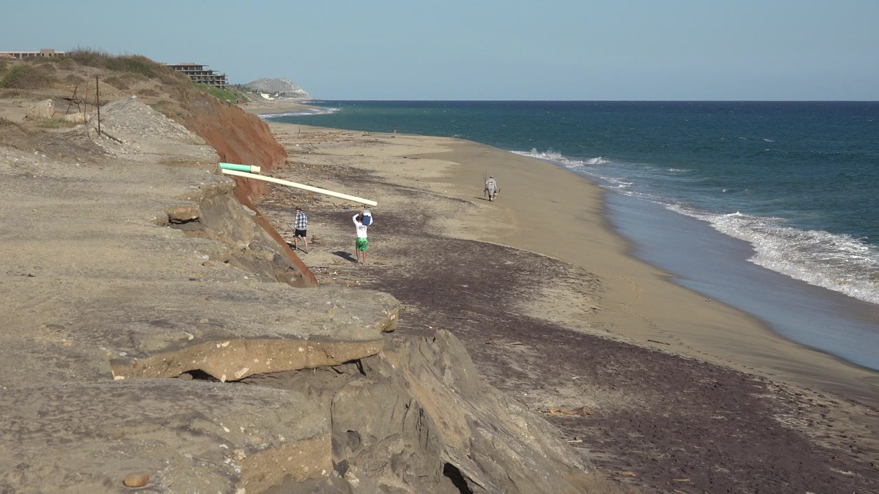 Two people walking on a sandy beach below cliffs with waves at right.