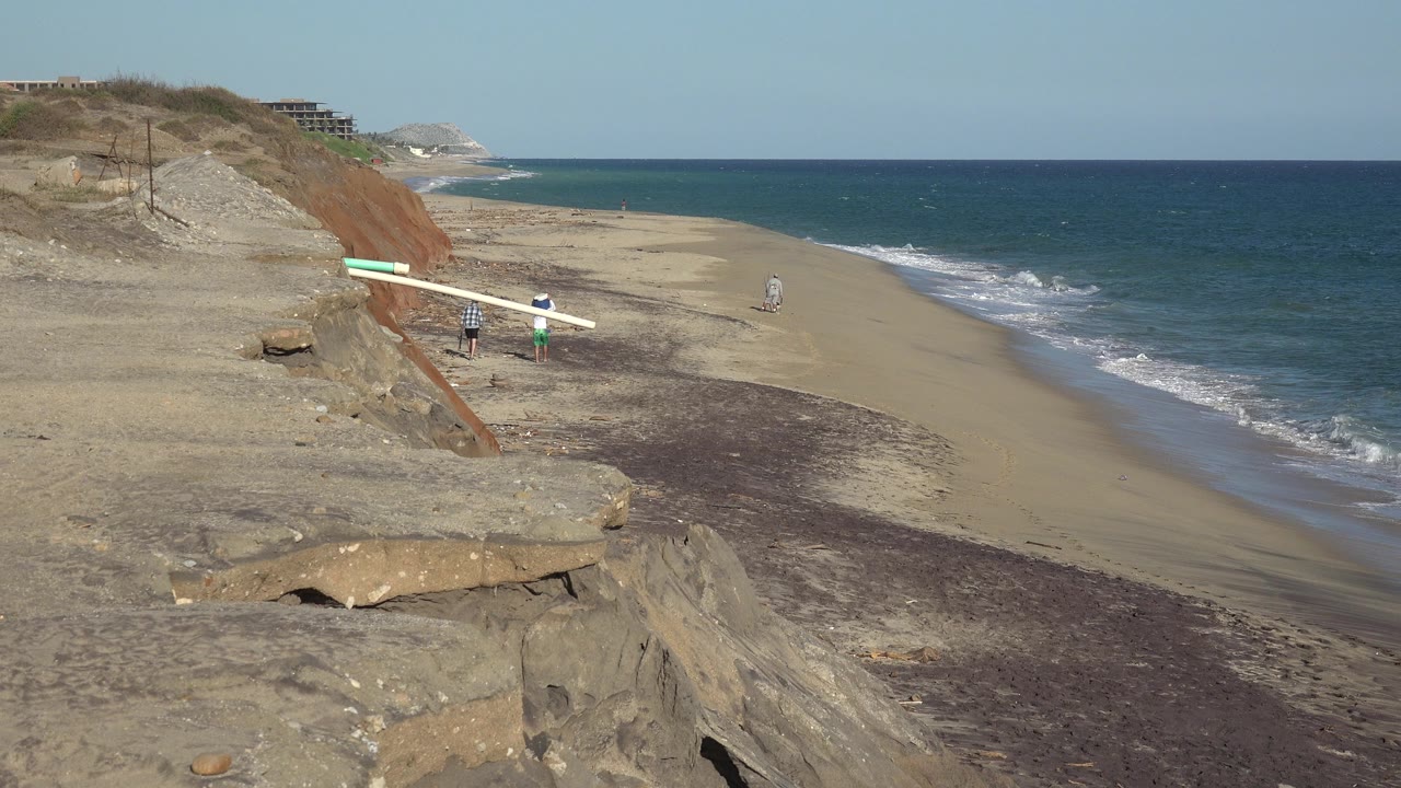 Wide beach below eroded bluffs with waves and small distant people.