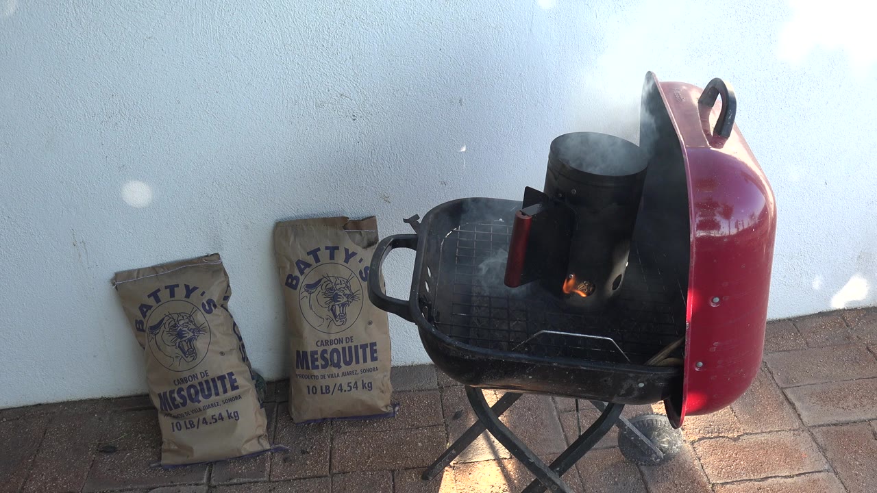 At 0:00 in Grand Junction, Colorado, a red open grill smokes beside two mesquite charcoal bags on a brick patio, with no visible people.