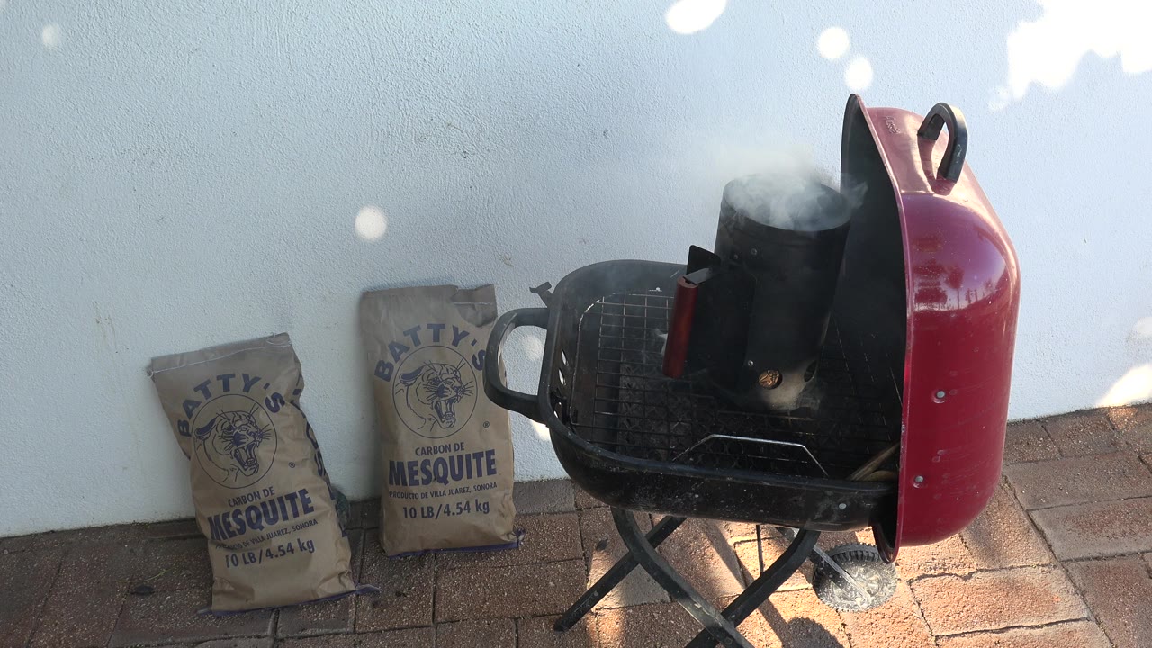 The chimney starter continues smoking on the red grill in Grand Junction, Colorado, with charcoal bags leaning against the wall and no visible people in the patio scene.