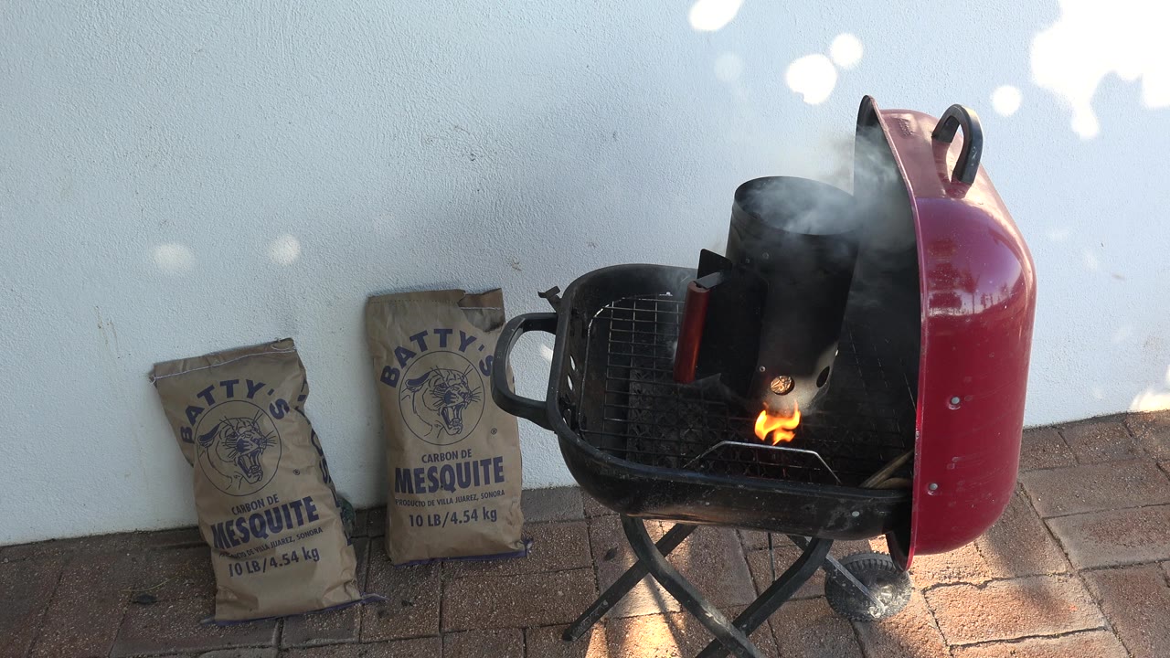 Small flame appears inside a chimney starter on a charcoal grill.