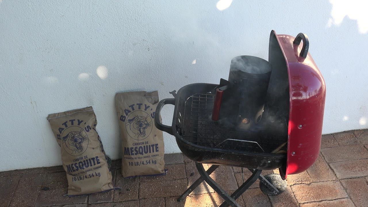 Red charcoal grill smoking beside mesquite charcoal bags
