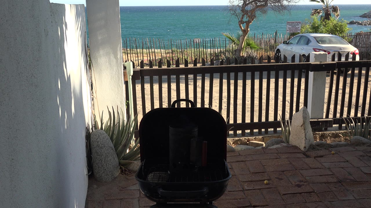 Shaded patio grill facing a fence, parked car, and blue water.
