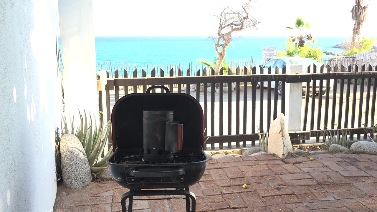 Open black barbecue on a brick patio with sea beyond a fence