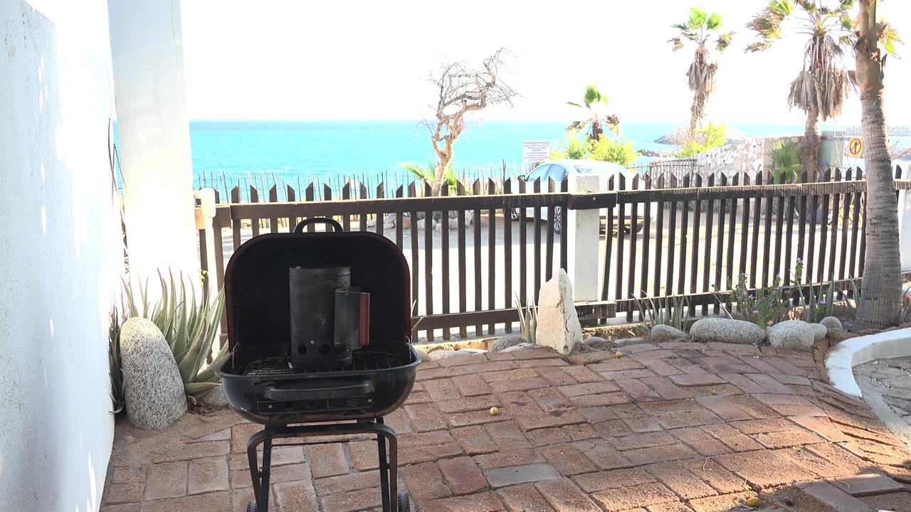 Black grill on a brick patio facing a fenced ocean view.