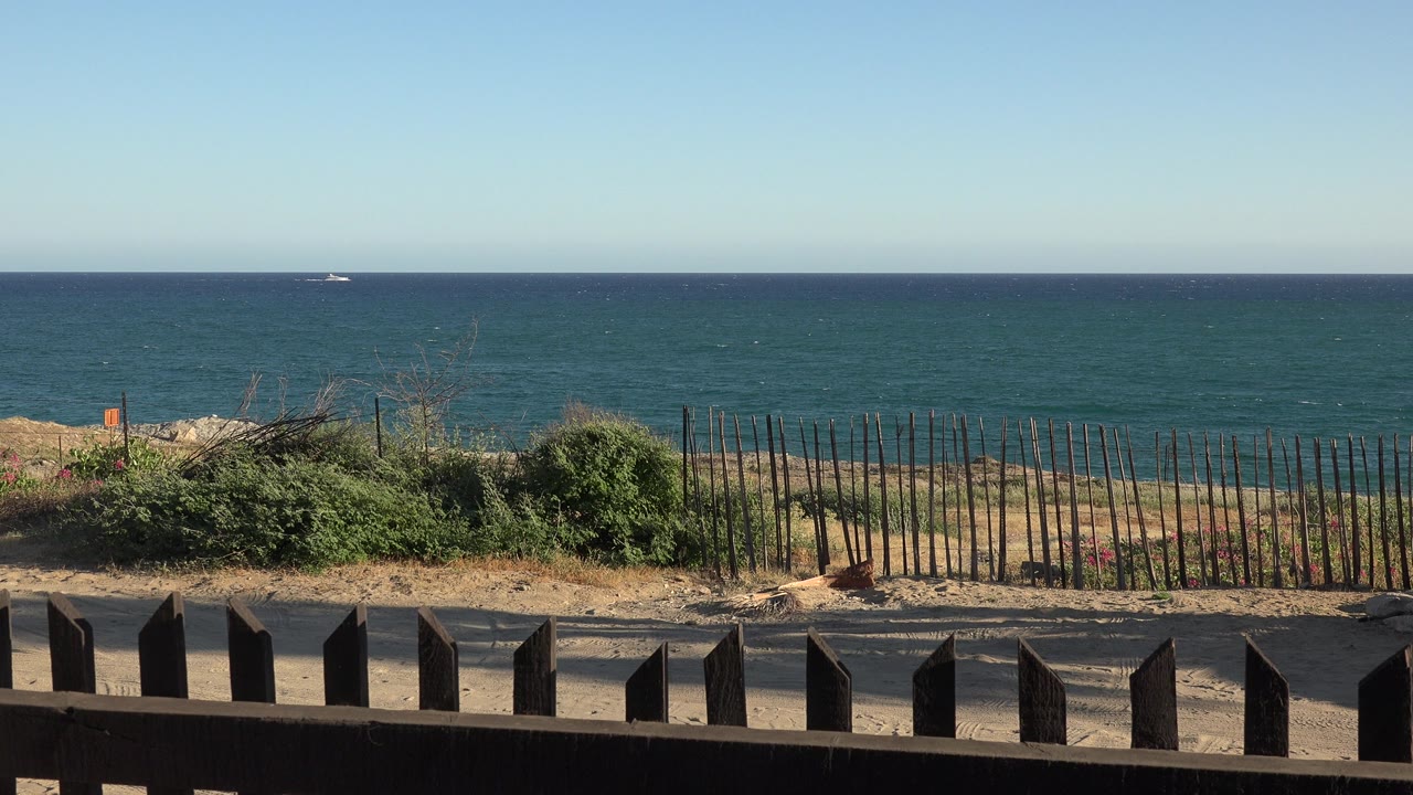 Ocean-like water beyond a roadside fence and wooden foreground railing.
