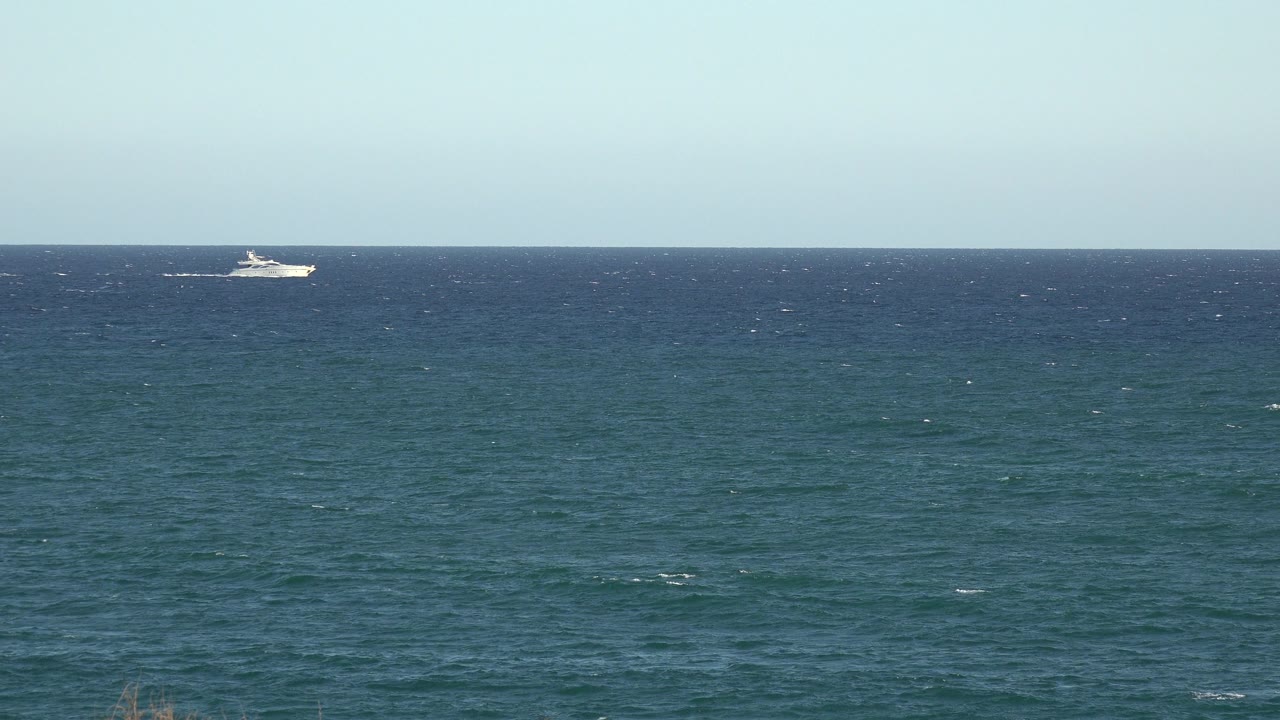 A small white boat appears near the left side of the horizon over blue-green water in Grand Junction, Colorado, with pale sky above and no visible people.