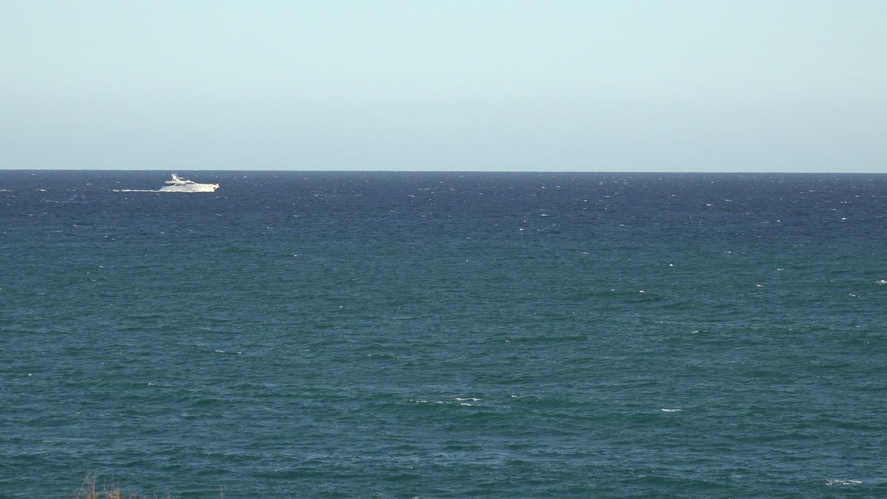 The distant white boat has moved closer to center-left along the horizon, with textured teal water below and no visible people in the Grand Junction, Colorado frame.