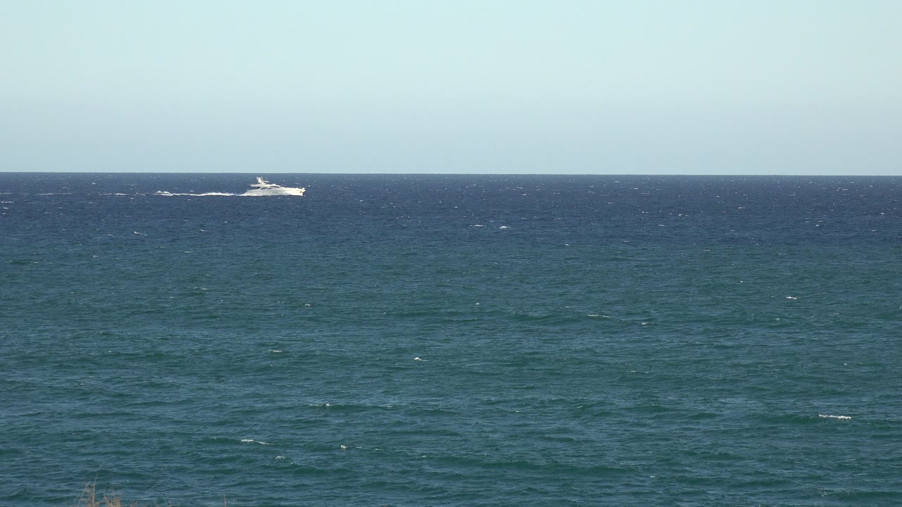 Distant white boat on a blue ocean horizon under pale sky.