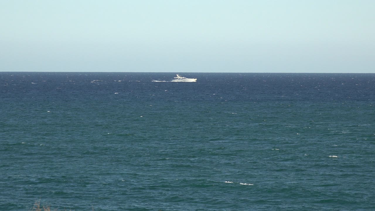 Distant white passenger ship on deep blue water under pale sky.