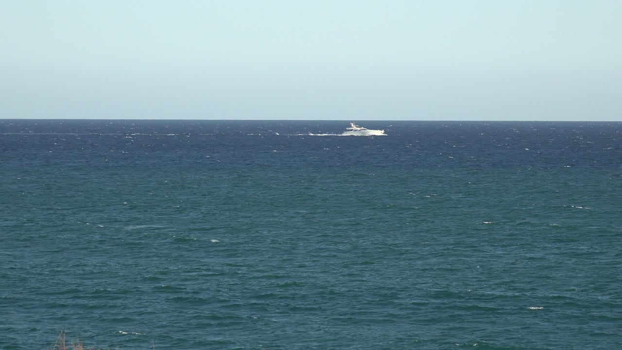 Distant white boat near the horizon on blue-green open water.