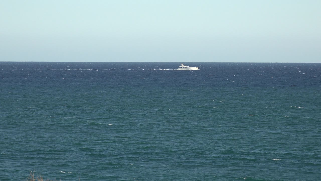 At 0:01, the distant white boat has moved along the horizon over textured blue-green water in the Grand Junction, Colorado 2017 footage, with no visible people.