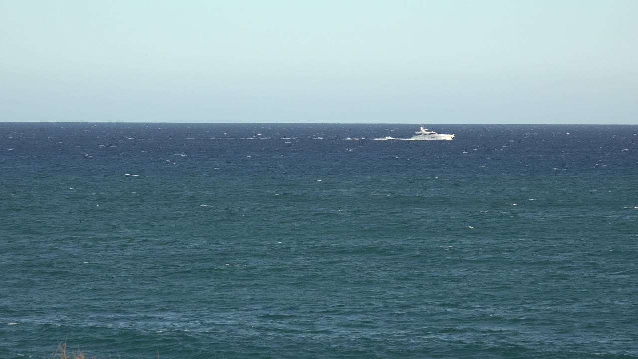 Small white boat near the horizon over blue-green water