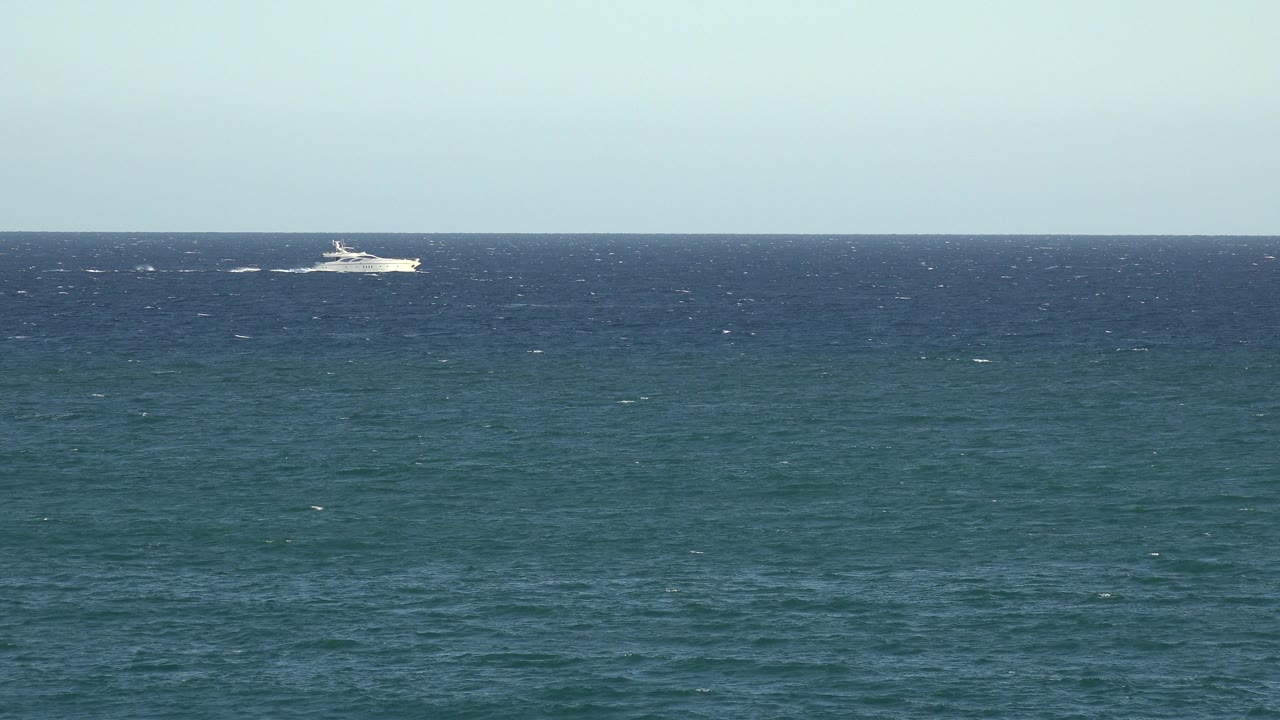 The white ship is positioned toward the right side of the horizon, leaving a pale wake behind it over the blue ocean, with no visible people in the frame.