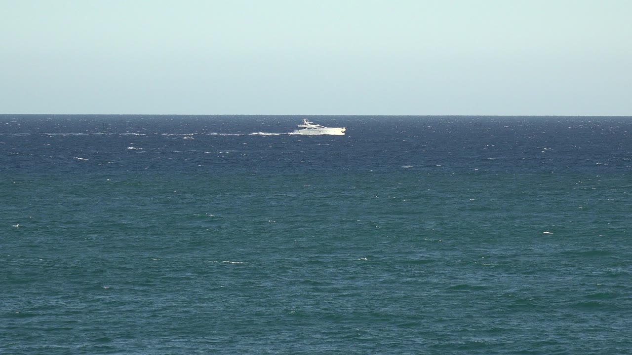 The white boat appears farther along the horizon line in Grand Junction, Colorado, with textured blue-green water in the foreground and no visible people.