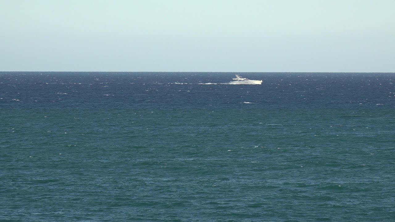At 0:01, the white vessel remains small near the horizon while short whitecaps mark the darker band of water, with no visible people.