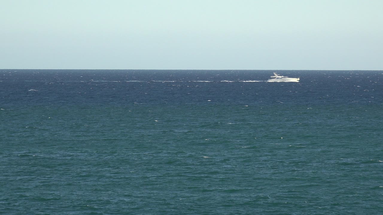 Wide blue sea and sky with a distant white boat near the horizon.