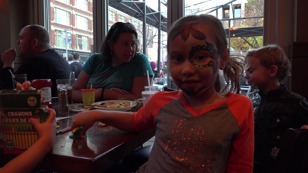 Face-painted girl at a table with adults and children nearby.
